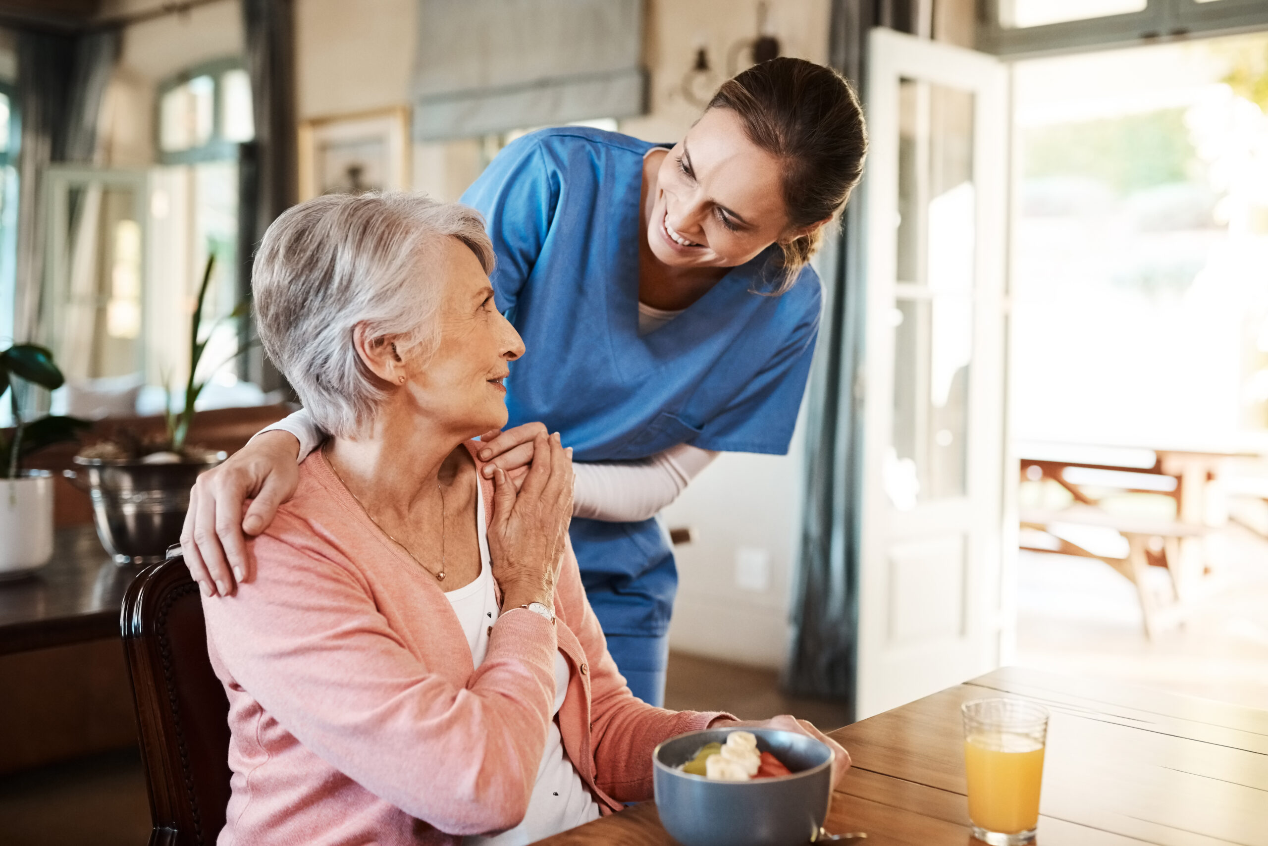 A young man lovingly embraces an elderly woman over breakfast.