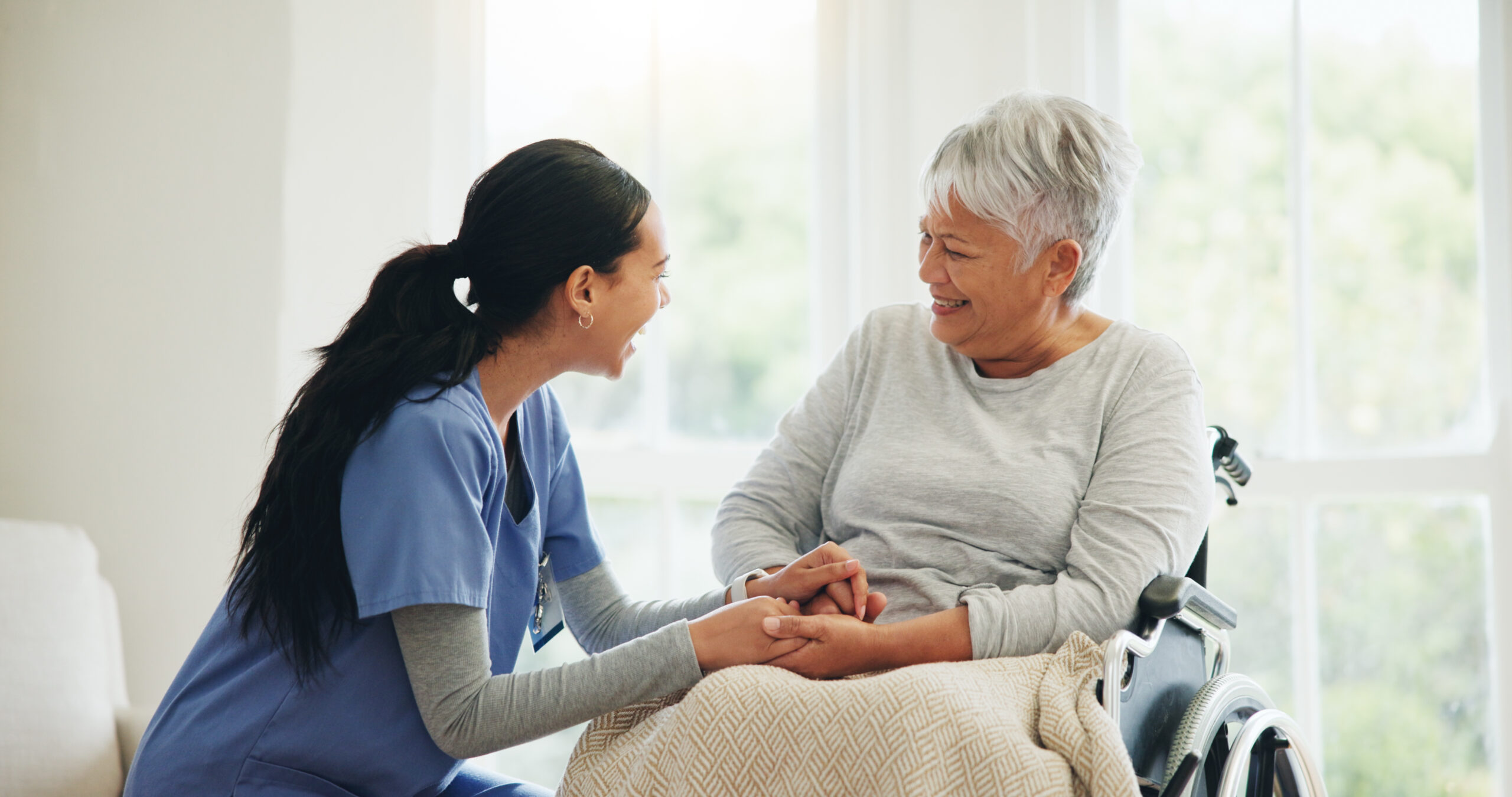 Nurse warmly holding elderly patient's hands during a caring conversation.
