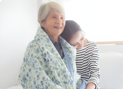 Elderly woman wrapped in a floral blanket with a young woman resting her head on her shoulder.