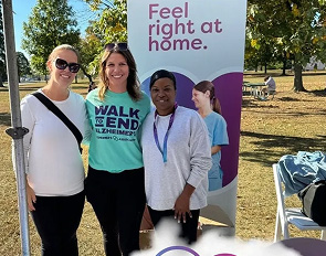 Three women smiling at an outdoor event with a 'Feel right at home' sign.