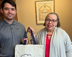 Two people holding a tote bag and smiling indoors.