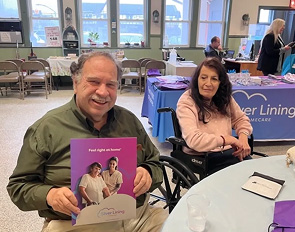 Two people smiling at a table, one holding a colorful booklet.