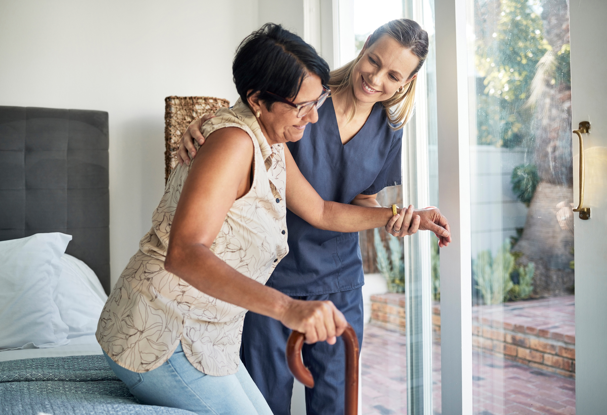 Caregiver assisting elderly woman to open a glass door at home.