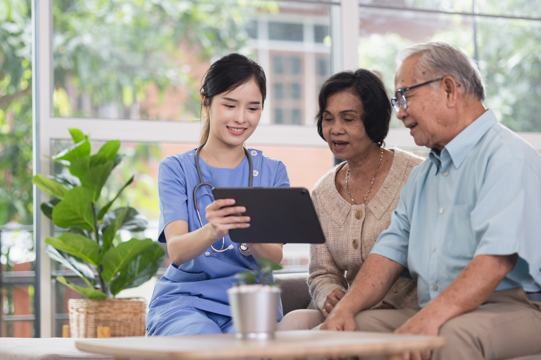 A young caregiver shows a tablet to an elderly couple.