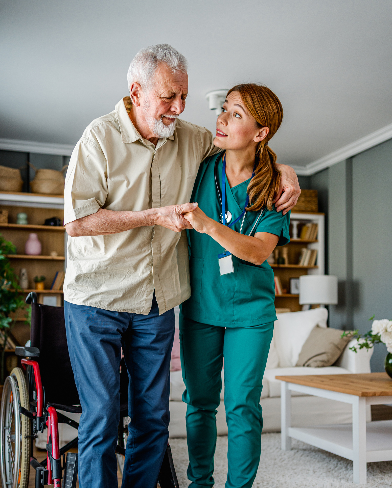 Caregiver assisting elderly man with walking indoors.