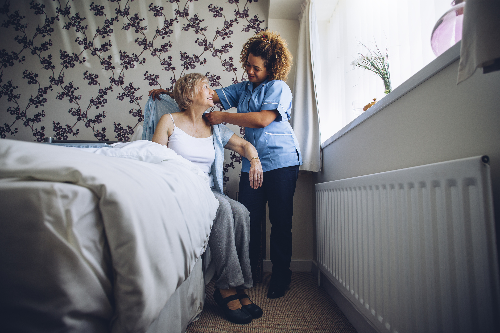 Caregiver assisting elderly woman to get out of bed.