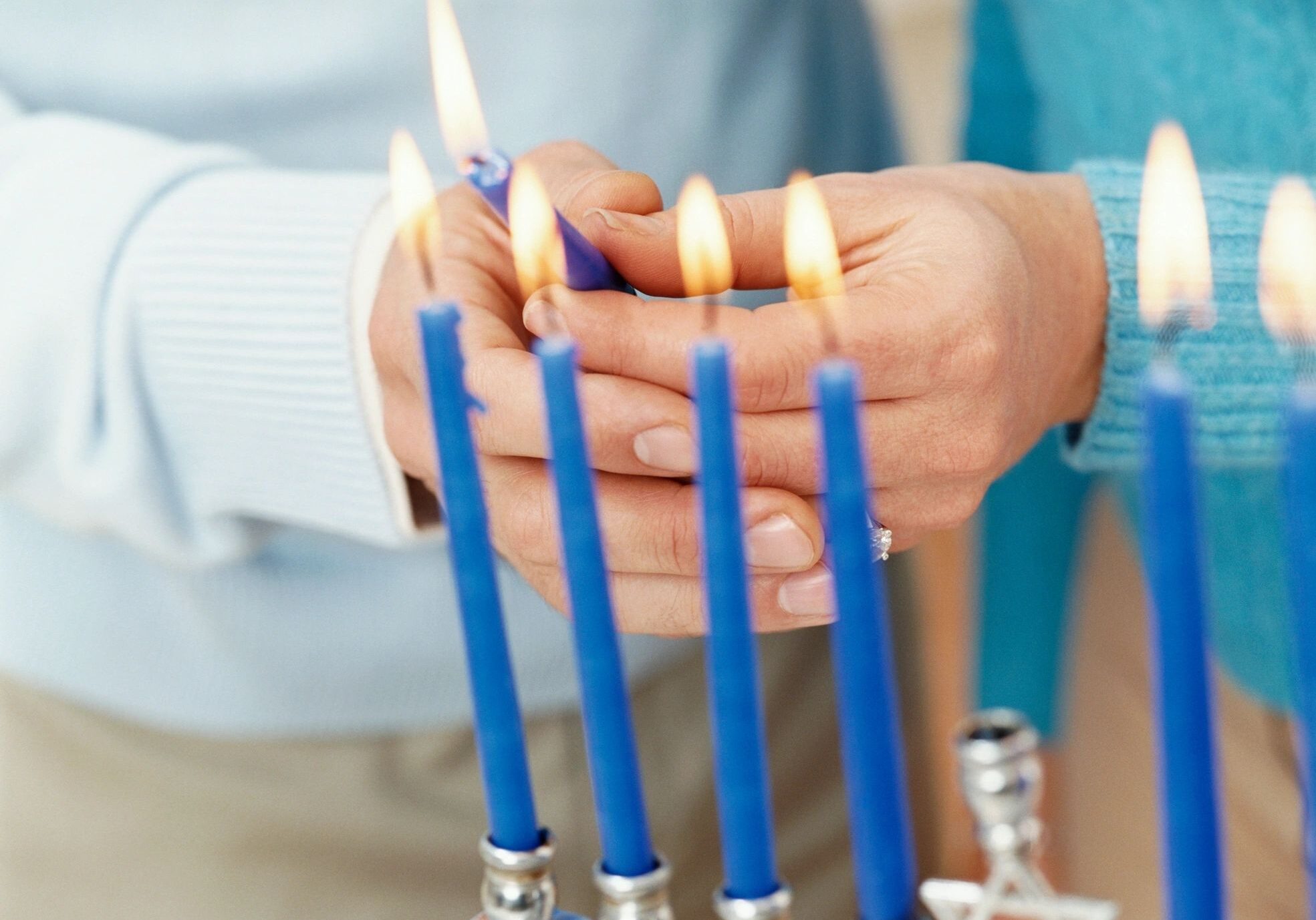 Hands lighting candles on a menorah.